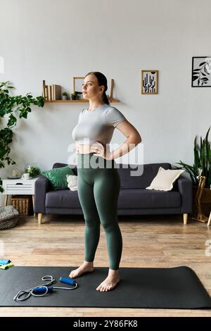 Die junge, sportliche Frau steht selbstbewusst auf ihrer Matte, bereit für ihr Heimtraining, das sich auf Bewegung konzentriert. Stockfoto