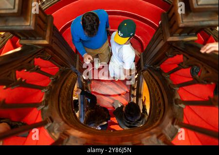 Porto, Portugal - 12. September 2024 : die Menschen bewegen sich über eine wunderschön gestaltete Wendeltreppe mit sattem rotem Teppich. Stockfoto