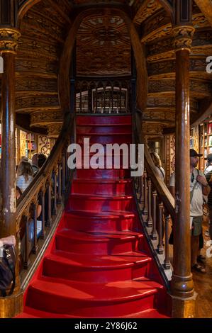 Porto, Portugal - 12. September 2024: Besucher erkunden einen charmanten Buchladen mit einer verzierten roten Treppe und Holzregalen Stockfoto