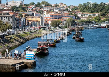 Porto, Portugal - 13. September 2024 : traditionelle Boote säumen das Ufer, während die Menschen einen sonnigen Tag am Fluss genießen. Stockfoto