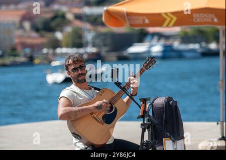 Porto, Portugal - 13. September 2024 : Ein talentierter Künstler spielt Gitarre und singt, während er an einem Ort am Wasser sitzt. Stockfoto