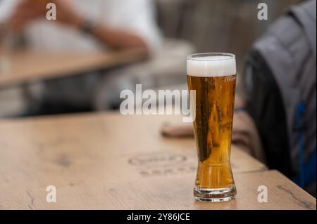 Porto, Portugal - 13. September 2024 : Ein erfrischendes Glas Bier steht auf einem Holztisch während einer lebhaften Veranstaltung im Freien. Stockfoto