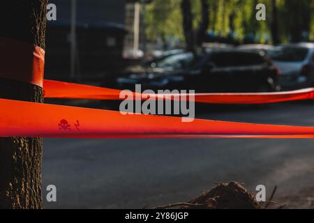 Nahaufnahme von rotem Warnband mit einem Schädel- und Kreuzknochensymbol, das um einen Baum gewickelt ist und einen Abschnitt der städtischen Straße absperrt Stockfoto