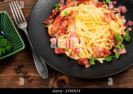 Pasta Carbonara mit Speck und Parmesan auf einem Teller auf einem alten rustikalen Holztisch. Italienisches Nudelgericht. Stockfoto
