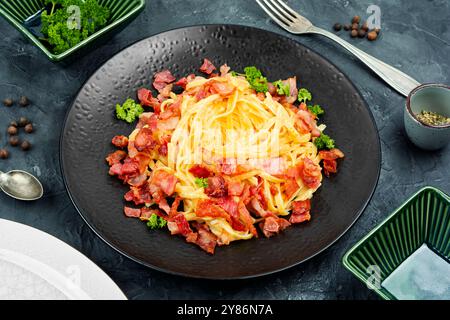 Hausgemachte Pasta mit gebratenem Speck, Pasta Carbonara serviert auf einem schwarzen Teller. Stockfoto