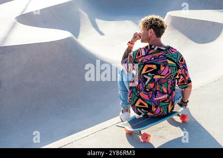Ein Typ mit buntem Hemd sitzt auf Skateboard Stockfoto