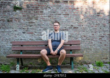 Sportlicher 45-jähriger Mann, der auf einer Bank sitzt, mit einer Ziegelsteinmauer im Hintergrund, Gréz, Brabant Wallon, Belgien. Modell freigegeben Stockfoto