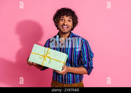 Porträt des netten jungen Mannes, der Geschenkschachtel trägt Hemd isoliert auf rosa Hintergrund Stockfoto
