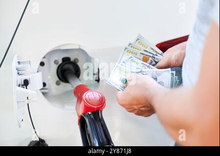 Ein Mann zählt Geld, das er für Treibstoff ausgeben muss. Transportkostenkonzept. Nahaufnahme eines Mannes, der Dollar zählt, vor dem Hintergrund des Betanks des Autos. Stockfoto