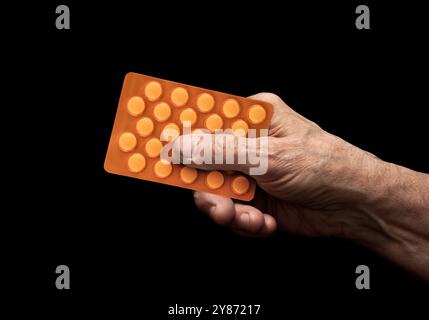 Arzneimittelpillen in der Seniorenhand über schwarzem Hintergrund Stockfoto