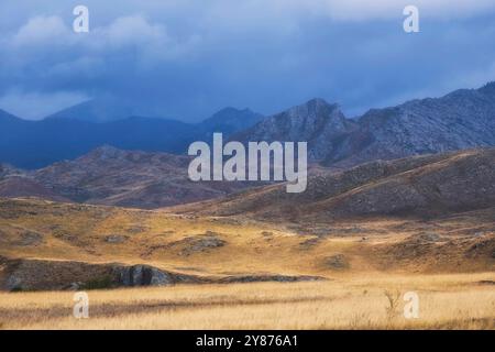 Wunderschöne herbstliche Berglandschaft in der Steppe mit trockenem gelbem Laub, Schokoladenhügeln und Felsen unter dunklem Himmel Stockfoto