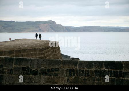 Zwei ferne Figuren auf dem Cobb bei Lyme Regis mit Blick auf das Meer, mit der Küste im Hintergrund Stockfoto