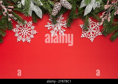 Roter Weihnachtshintergrund mit Tannenzweigen und rosa Weihnachtsbaumspielzeug und Schneeflocken Stockfoto