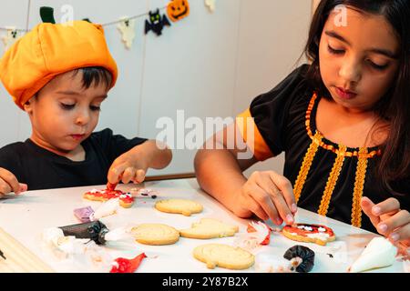 Ein Mädchen und ein Junge machen Halloween-Kekse. Das Mädchen trägt ein schwarzes Kleid und der Junge ein schwarzes Hemd Stockfoto