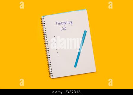 Einkaufsliste handgeschrieben auf einer weißen Seite eines Notizblocks und einem blauen Marker auf gelbem Hintergrund mit Kopierraum Stockfoto