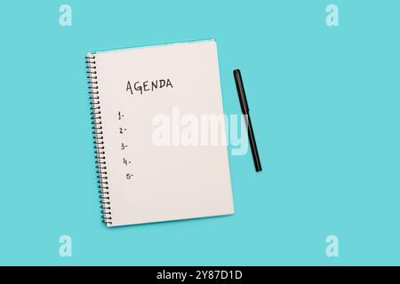 Tagesordnungspunkt handgeschrieben auf einer weißen Seite eines Notizblocks mit schwarzem Marker auf hellblauem Hintergrund mit Kopierraum Stockfoto