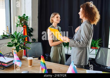 Zwei Kollegen teilen einen freudigen Moment in ihrer integrativen Büroumgebung, umgeben von Fahnen. Stockfoto