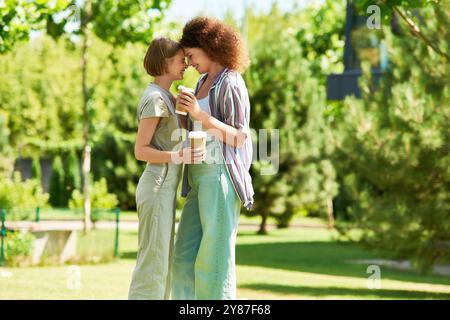 Zwei Freunde verbringen einen fröhlichen Moment in einem lebhaften Park, schlürfen Smoothies und lächeln einander an. Stockfoto