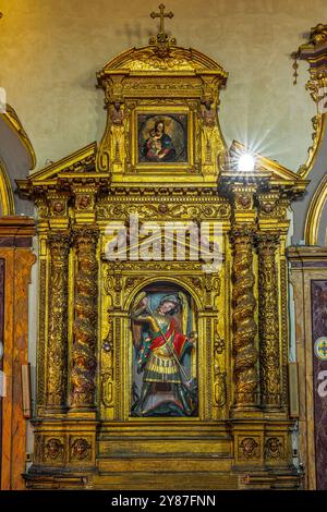 Der vergoldete geschnitzte Holzaltar mit verdrehten Säulen und die polychrome Holzskulptur des Erzengels Michael in der Stiftskirche. Abruzzen Stockfoto