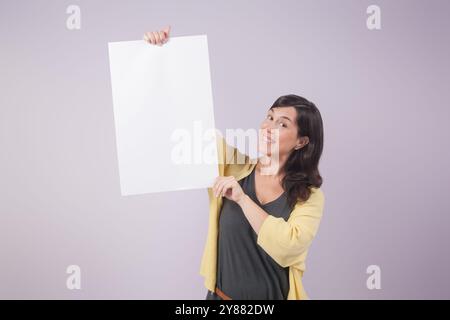 Eine Frau hält ein leeres Schild und lächelt. Das Schild ist weiß und hat keine Aufschrift. Der Ausdruck der Frau deutet darauf hin, dass sie glücklich und aufgeregt ist Stockfoto