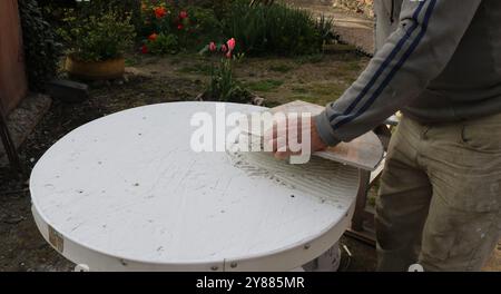 Ein Handwerker legt ein Stück Fliese, das aus einer Schablone geschnitten wurde, auf eine runde Tischplatte, die mit einer Mörtelschicht bedeckt ist Stockfoto