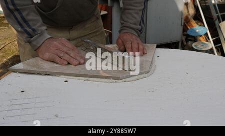 Der Fliesenleger legt Keramikfliesen mit Mörtel auf die Oberfläche des Produkts und legt ein Eisengewicht an, um sie zu einem runden Tisch zu ebnen Stockfoto