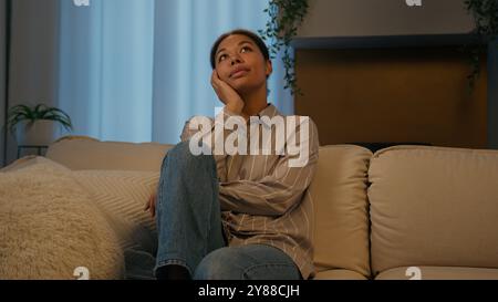 Afroamerikaner verträumte Frau ethnisch ruhiges Mädchen träumt auf Couch Sofa am Abend zu Hause entspannte friedliche Hausbesitzerin, die nebendenkt Stockfoto