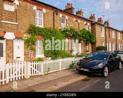 Tesla Elektroauto parkte auf der Straße vor einer Reihe viktorianischer Reihenhäuser mit weißem Holzpfahlzaun in Gentleman's Row, Enfield, London, Stockfoto