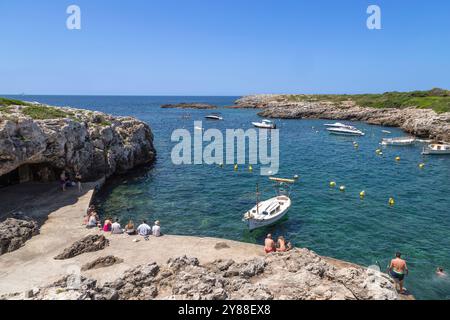 Die Menschen sitzen und schwimmen im kleinen Hafen des Küstendorfes Binibequer Vell auf der spanischen Insel Menorca. Stockfoto