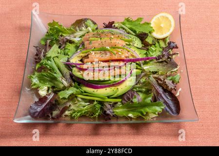 Köstlicher Salat mit Lachsscheiben, Zwiebeln, Avocado Rucola und einer Zitrone Stockfoto