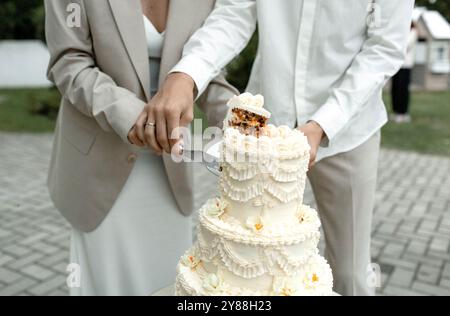 Eine wunderschön gefertigte Hochzeitstorte steht hoch und zeigt komplizierte Rüschen und Blumenakzente, eingerahmt von einer bezaubernden weißen Blütenpracht Stockfoto