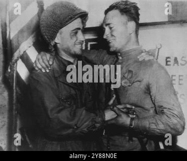 Yank und Russen umarmen sich, als sich Armeen treffen -- Zweiter Lt. William D. Robertson (links), aus Los Angeles, Kalifornien, 69. Infanteriedivision, erste US-Armee, und Lt. Alexander Sylvashko von der russischen Armee, umarmte vor einer gerollten amerikanischen Flagge und einem unhöflichen Schild "Ost trifft Westen", als die Yanks und die Sowjets am 25. April einen Knotenpunkt durch Deutschland am Ostufer der Elbe bildeten. April 1945. (Foto von Associated Press Radio Photo). Stockfoto