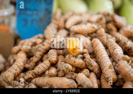 Ein Haufen Kurkuma-Wurzeln auf einem Stand zum Verkauf. Einer von ihnen ist aufgeschnitten. Stockfoto