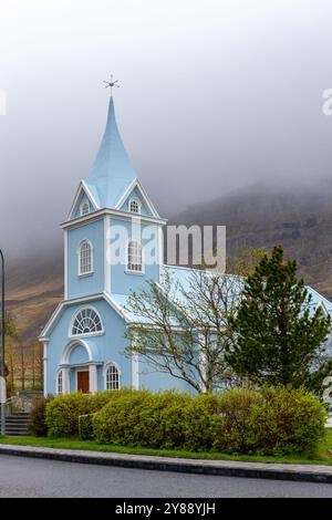 Die Blaue Kirche in Seydisfjordur (Seydisfjardarkirkja), Außenansicht der hellblauen Gebäudefassade mit grüner Vegetation rund um Island. Stockfoto