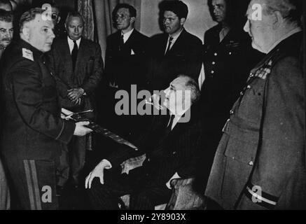 Präsident Roosevelt sieht Stalingrad-Schwert auf der Historischen Teheran-Konferenz -- Klementy E. Woroshilow, Marschall der Sowjetunion, zeigt Präsident Franklin. D. Roosevelt von den USA (sitzend) ein Schwert, das von Premierminister Winston Churchill von Großbritannien (rechts) Marschall Joseph Stalin (äußerste Linke), dem Premierminister der Sowjetunion, als Zeichen der Hommage des britischen Volkes für Stalingrads heldenhaften Widerstand gegen die Deutschen bei einer Zeremonie in Teheran, Iran, überreicht wurde, wo die alliierten Führer Operationen zur Vernichtung der deutschen Streitkräfte absprachen. Hinter Stockfoto
