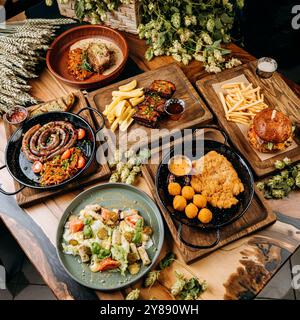 Blick von oben auf Gourmetgerichte wie Würstchen, Rippchen, Schnitzel, Salat und Burger auf dem Tisch Stockfoto
