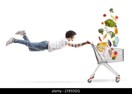 afroamerikaner fliegt und hält einen Einkaufswagen mit Lebensmitteln, die auf weißem Hintergrund fallen Stockfoto