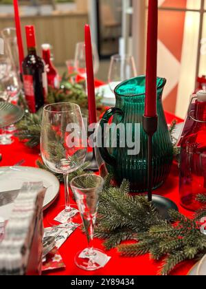 Der festliche Weihnachtstisch ist mit festlichen Dekorationen geschmückt und bereit für ein fröhliches Treffen im Winter. Leuchtend rote Tischdecke und elegantes Geschirr Stockfoto