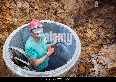 Zementstaub blendete den Klärgrubenbauer, als er mit einem Winkelschleifer mit Diamanttrennscheibe ein Loch in den Betonring sägte. Stockfoto