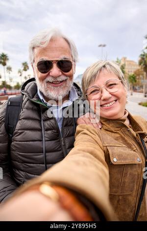Vertikal. Ein paar lächelnde ältere kaukasische Touristen, die zusammen Selfie machen. Ehemann und Frau verliebt Stockfoto