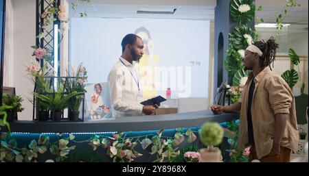 Der Store Manager spricht mit dem Kunden im Bekleidungsgeschäft und erklärt die Schritte des Erstattungsverfahrens, nachdem er gekaufte Kleidung zurückgegeben hat. Der Mitarbeiter im Einzelhandel macht Notizen, während der Kunde persönliche Informationen gibt Stockfoto