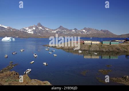 Blick auf kleine Boote im ruhigen Fjord, mit Bergen und farbenfrohen Häusern im Hintergrund, Knud Rasmussen Gletscher, Tasilaq, Ostgrönland, Dänemark, Eu Stockfoto