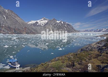 Ein kleines Boot, das auf einem klaren Fjord vor einer beeindruckenden Berg- und Gletscherlandschaft liegt, Knud Rasmussen Gletscher, Tasilaq, Ostgrönland, Denmar Stockfoto