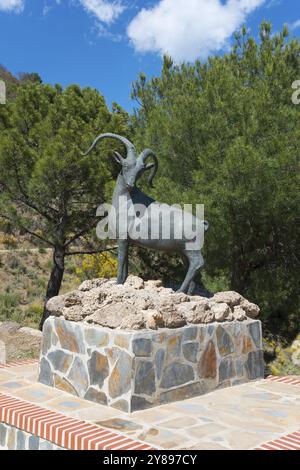 Bronze-Steinbock-Statue auf einem Backsteinsockel umgeben von grünen Bäumen, Gegend Recreativa de Sedella, Parque Natural de las Sierras de Tejeda, Almijara und Alham Stockfoto