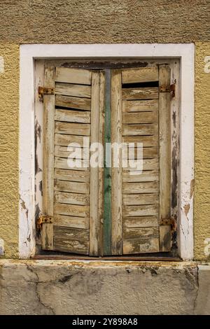 Weiße alte Holzfenster mit grauen Fensterläden an der gelben Hausfassade Stockfoto