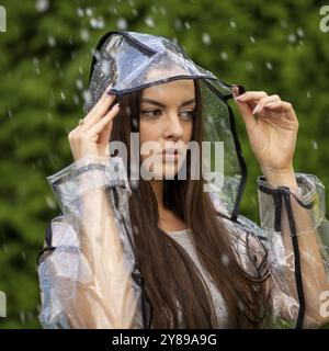 Junge schöne Frau im Regenmantel mit Kapuze an regnerischen Tagen Stockfoto