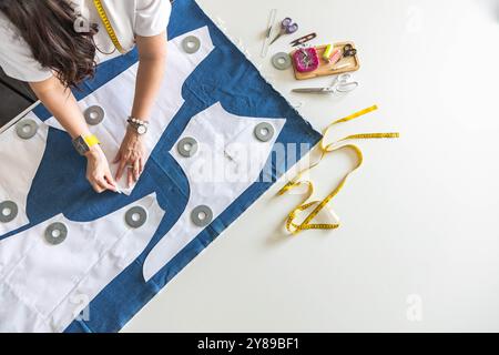 Eine Schneiderin legt Musterdetails auf Denim und schneidet Kleidung. Draufsicht. Stockfoto