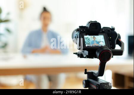 Auf einem Kamerabildschirm sitzt eine hübsche indische oder arabische brünette junge Frau, Blogger, Influencer an einem Schreibtisch, schaut sich die Kamera an, nimmt Lernvlog auf, Videokurs für soziale Medien Stockfoto
