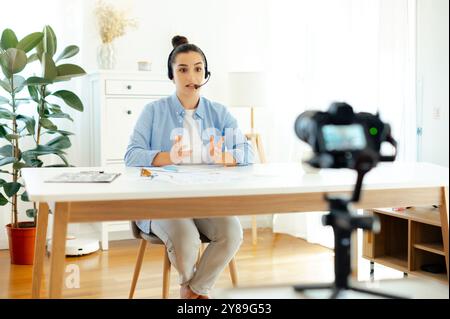 Online-Videokurs. Hübsche kaukasische brünette junge Frau, Coach, Blogger, Influencer sitzt an einem Schreibtisch, schaut in die Kamera, nimmt Lernvlog auf, Videokurs für soziale Medien, Webinar Stockfoto