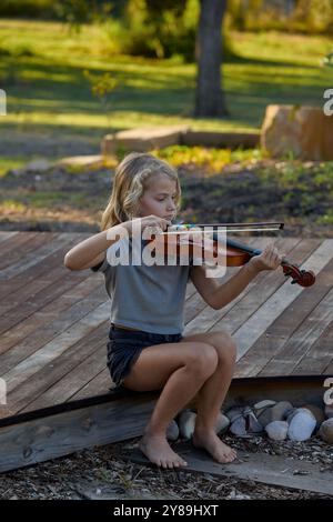 Das Mädchen spielt Geige, während es auf einem Deck sitzt Stockfoto